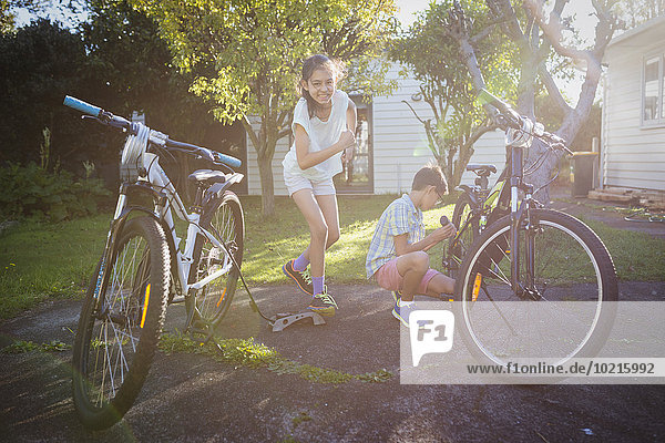 Mixed race children fixing bicycles in backyard