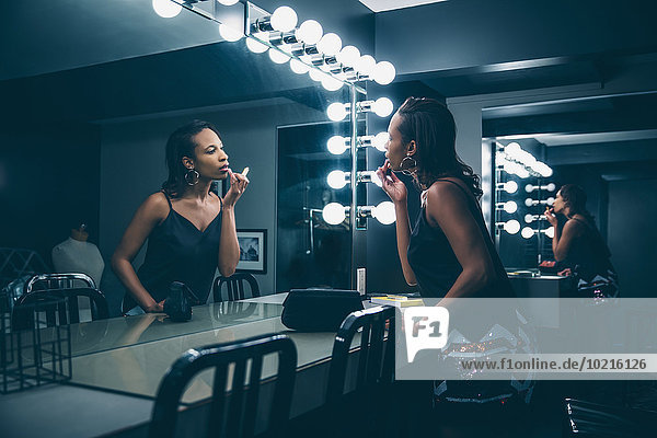 Black woman applying makeup in vanity mirror