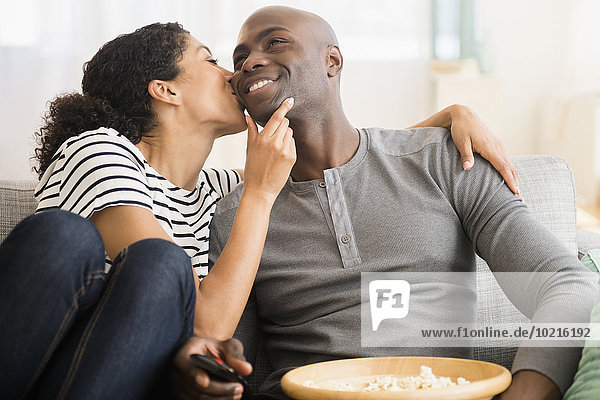 Smiling couple watching television on sofa