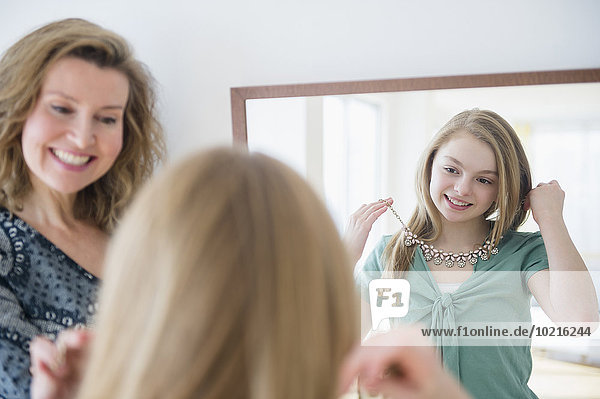 Caucasian girl examining necklace in mirror with mother