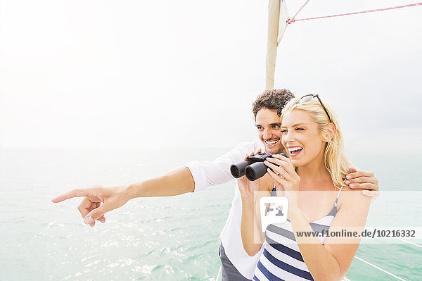 Couple looking out from boat deck with binoculars