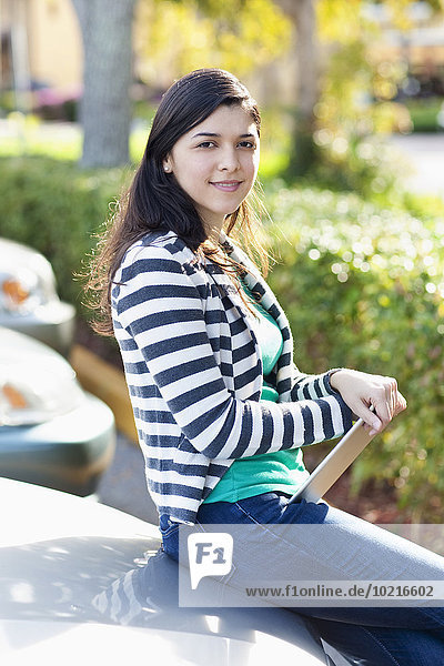 Hispanic woman holding digital tablet in parking lot