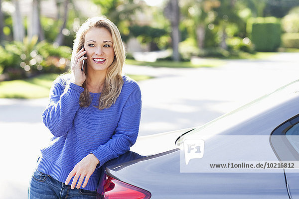 Caucasian woman talking on cell phone at car