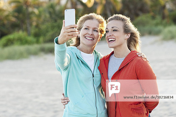 Caucasian mother and daughter taking selfie on beach