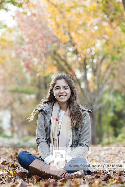Hispanic girl sitting in autumn leaves