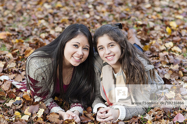 Hispanic sisters laying in autumn leaves