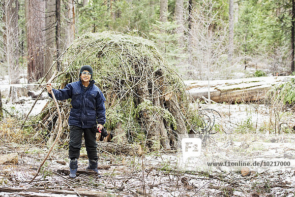 Hispanic boy building hut from branches in forest