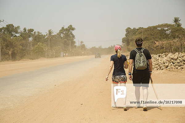 Caucasian couple walking on dirt road in remote field