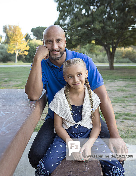 Father and daughter smiling on picnic table in park
