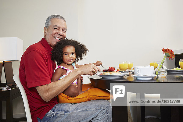 Grandfather and granddaughter eating breakfast at table