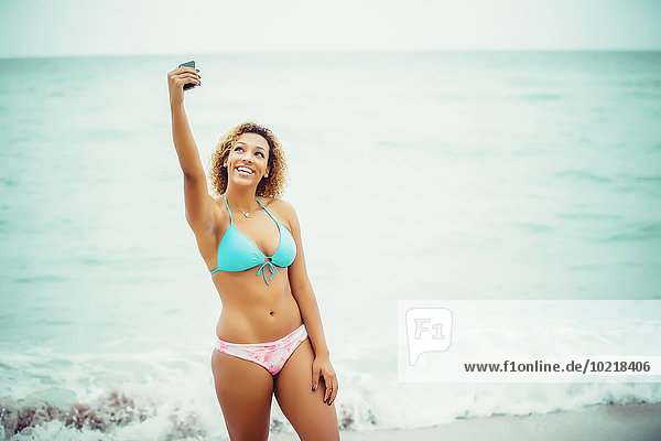 Mixed race teenager taking selfie in bikini on beach