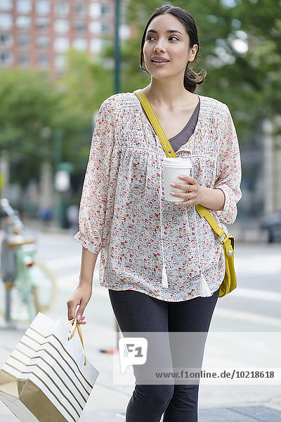 Hispanic woman carrying shopping bag on city sidewalk