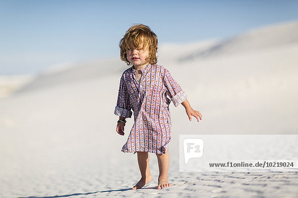 Caucasian baby boy walking on desert sand dune