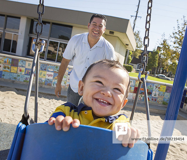 Hispanic father pushing son on playground swings