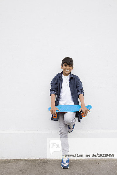 Asian boy holding skateboard at wall