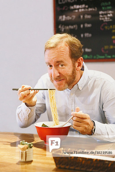 Caucasian man with beard eating ramen noodles