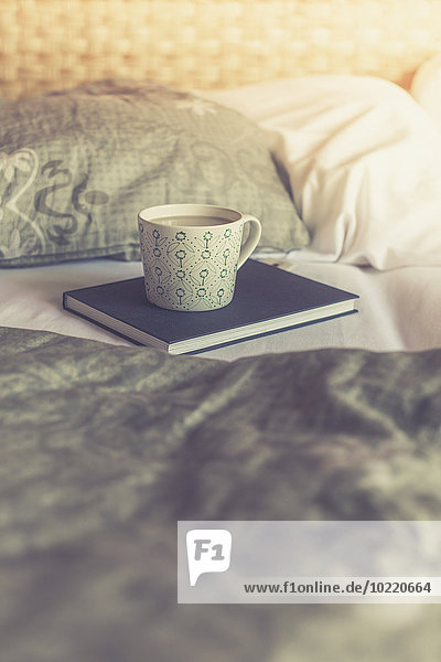 Buch und Tasse weißer Kaffee auf einem Bett