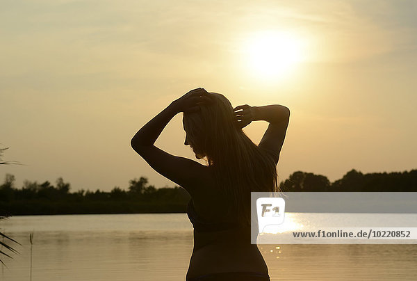 Deutschland  Brandenburg  Silhouette einer jungen Frau vor einem See im Gegenlicht