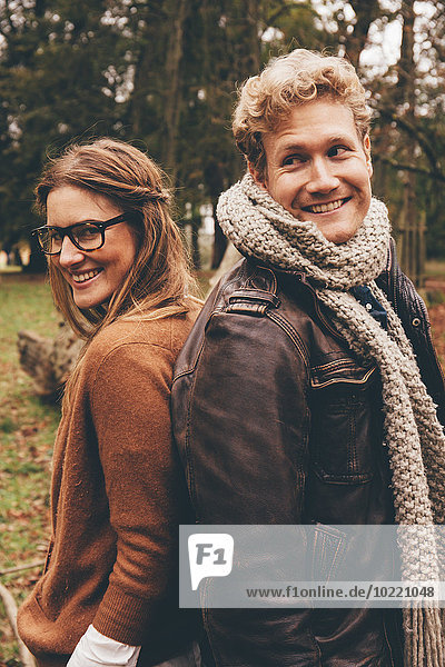 Happy young couple standing back to back in an autumnal park