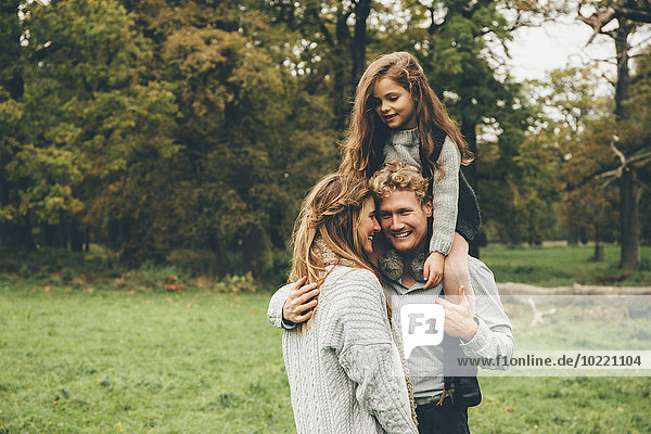 Young couple with little girl on her father's shoulders at autumnal park