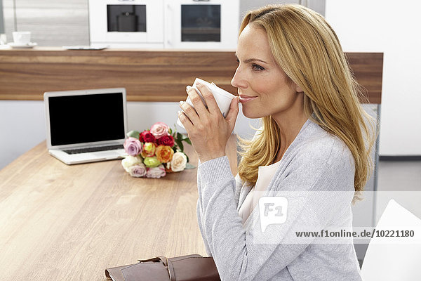 Lächelnde Frau  die Kaffee trinkt  während sie am Tisch sitzt und wegschaut.