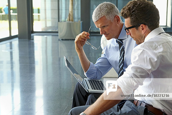 Zwei Geschäftsleute bei der Arbeit am Laptop in der Bürolobby