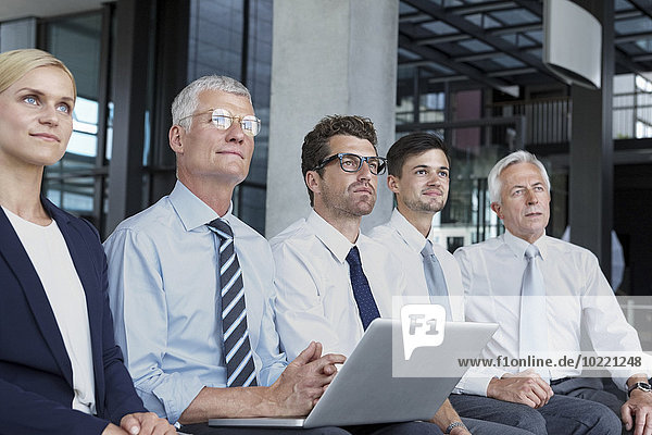 Group of businesspeople sitting in a row looking up