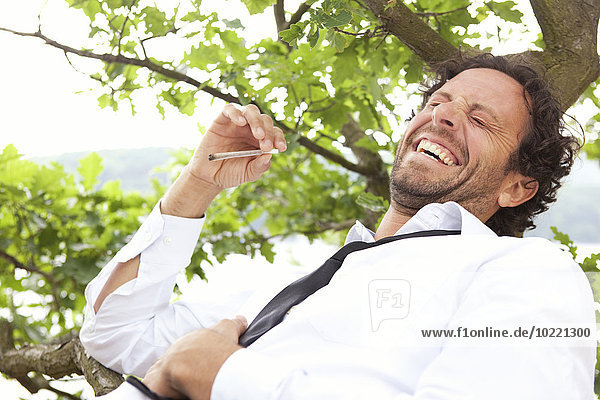 Germany relaxed businessman lying in tree smoking a joint