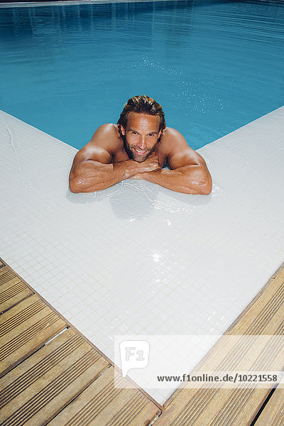 Porträt eines lächelnden Mannes im Schwimmbad  der sich an den Beckenrand lehnt.