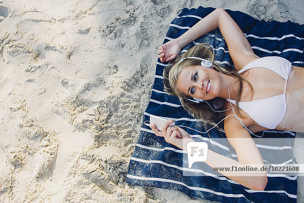 Lächelnde Frau beim Entspannen und Musik hören am Strand