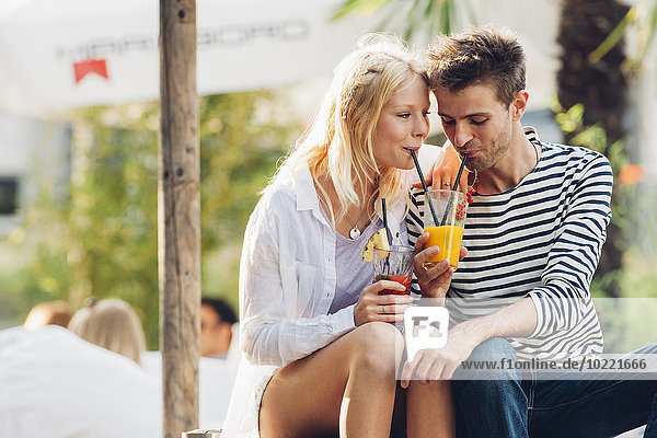 Young couple drinking fruit juice together at outdoor cafe
