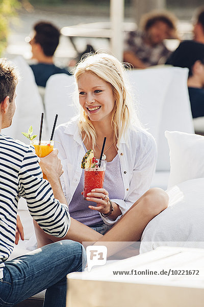 Porträt einer glücklichen jungen Frau mit einem Glas frischem Saft  die mit ihrem Freund in einem Straßencafé sitzt.