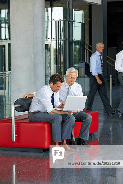 Zwei Geschäftsleute bei der Arbeit am Laptop in der Bürolobby