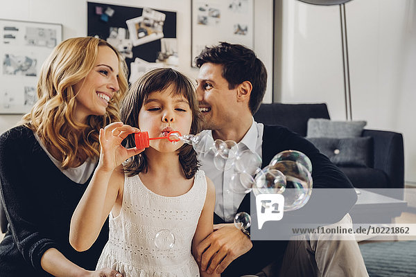 Happy family at home with girl blowing soap bubbles