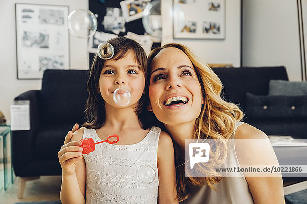 Happy mother with daughter at home blowing soap bubbles