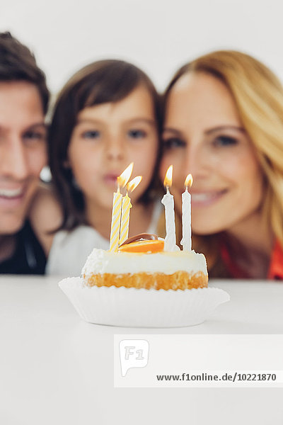 Kindergeburtstag mit Kerzen auf Kuchen und Familie im Hintergrund