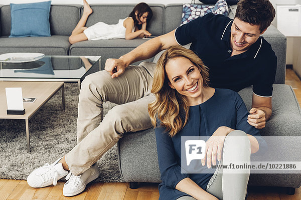 Smiling couple in living room with daughter using digital tablet in background