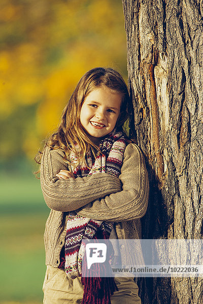 Portrait of smiling girl leaning on tree trunk