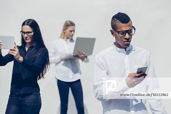 Drei stilvolle junge Leute mit Mini-Tablett  Smartphone und Laptop vor weißem Hintergrund