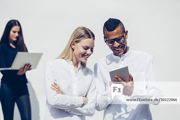 Lächelnde junge Frau und Mann betrachten Mini-Tablett vor weißem Hintergrund