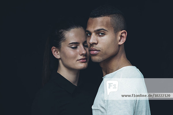 Porträt des jungen Paares Kopf an Kopf vor schwarzem Hintergrund
