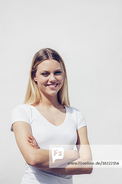 Porträt einer lächelnden jungen Frau mit gekreuzten Armen vor weißem Hintergrund