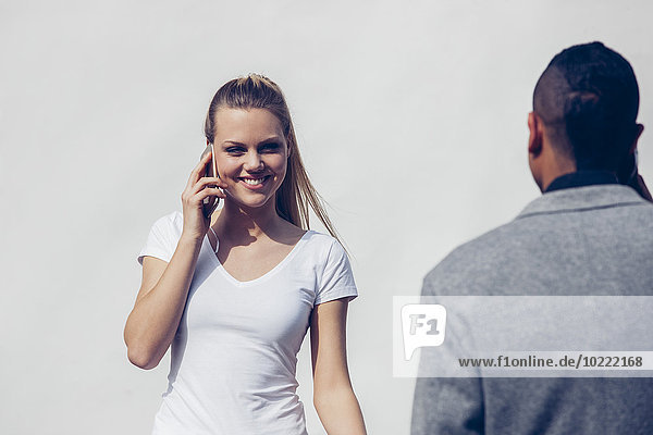 Porträt einer jungen Frau beim Telefonieren mit Smartphone vor weißem Hintergrund