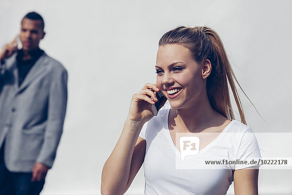 Portrait of smiling young woman telephoning with smartphone in front of white background