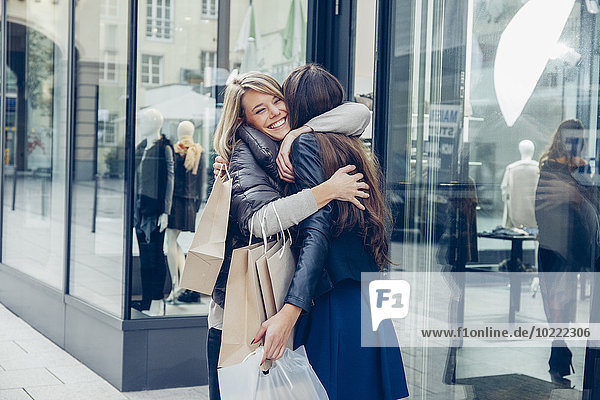 Zwei glückliche junge Frauen mit Einkaufstaschen  die sich vor einem Laden umarmen.