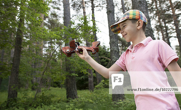 Junge spielt mit Holzflugzeug im Wald