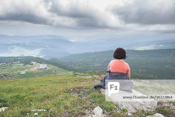 Bulgarien  Rila-Gebirge  Rückansicht einer älteren Frau  die auf einem Felsen sitzt und die Aussicht betrachtet