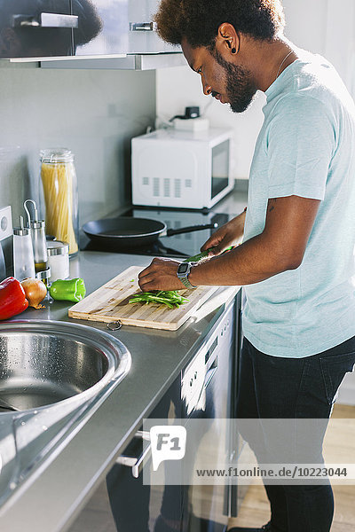 Junger Mann schneidet Gemüse in seiner Küche