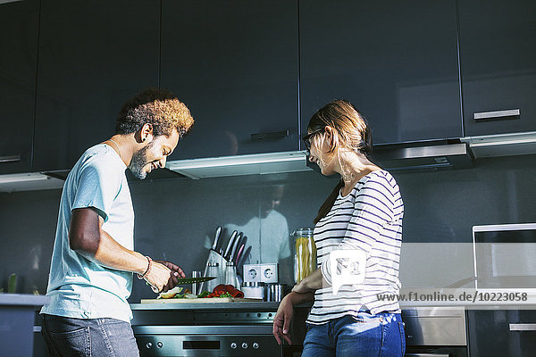 Junger Mann kocht in der Küche  während die Frau ihn beobachtet.