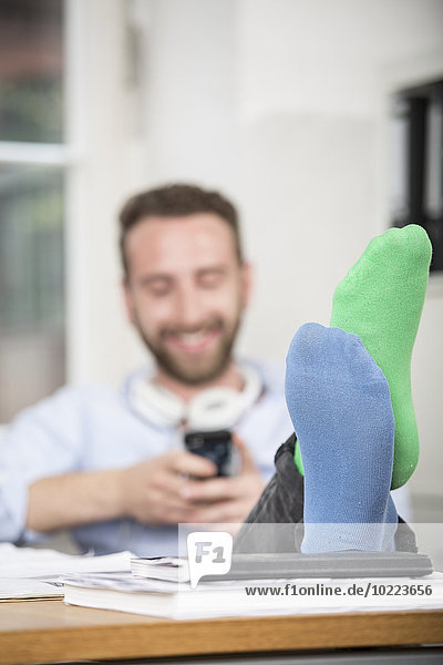 Junger Mann im Büro mit Füßen auf dem Schreibtisch in verschiedenen Socken